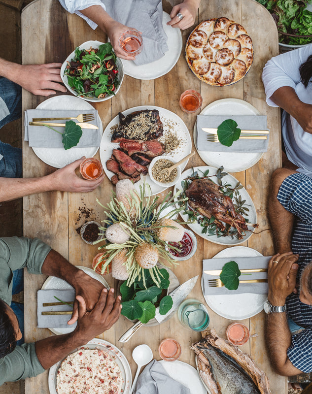 Warndu table with mixed race family seated around food infused with Australian Native Food aka Bush Tucker or Bush Foods only the hands of the family can be seen. 